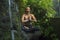 Outdoors adventure portrait of young beautiful and happy woman doing yoga and meditation exercise sitting in lotus posture on rock