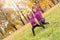 Outdoors leisure. Sisters doing lunge exercise hands up in the autumn park looking aside joyful