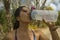 Outdoors lifestyle portrait of young attractive tired and thirsty Asian woman drinking water after hard running workout cooling