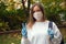 Outdoors portrait of beautiful young woman wearing cotton white mask and medicalgloves greeting and say hello, Nature and trees in