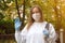 Outdoors portrait of beautiful young woman wearing cotton white mask and medicalgloves greeting and say hello, Nature and trees in