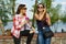 Outdoors portrait of female friends drinking coffee and having fun. Background nature, park, river. Urban lifestyle and friendship