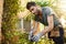 Outdoors portrait of young attractive bearded hispanic man in blue t-shirt and gloves working in garden with tools