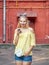 Outdoors portrait of young beautiful blonde woman with high bun hairstyle jeans shorts yellow blouse enjoying chatting on smartpho