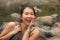 Outdoors portrait of young beautiful and happy Asian Chinese woman carrying backpack trekking on mountains crossing river enjoying