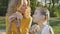 Outdoors portrait of young blonde mother eating cheeseburger sitting on the bench in the park with her little daughter