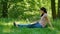 Outdoors Portrait of Young Brunette Woman with White Laptop Sitting on Green Grass in the Park and Working with Pleasure