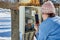 Outdoors switchboard with electric meter, woman takes readings using smartphone in winter.