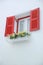 Outer opened red and white inner closed window with white wall decorated with flowerpod