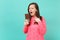 Outraged irritated young woman in knitted pink sweater hold in hand, looking on chocolate bar isolated on blue turquoise