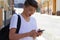 Outside portrait of teen boy. Handsome teenager carrying backpack on one shoulder and smiling, communicating by phone.