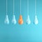 Outstanding orange light bulb hanging among light blue light bulb on blue background.