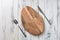 Oval cutting board with knife and fork on white wooden background