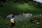 Oval mountain lake among alpine meadows. Female hiker looks at lake. Girl travels in summer through mountains of Caucasus with her