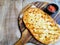 Oval Shape Cheesy Flatbread with Salsa Dip on a Round Wooden Pizza Board with Handle on a Wooden Table