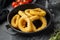 Oven baked breaded calamari rings on cast iron frying pan skillet, on black dark stone table background