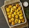 Oven baked whole crushed and crusty potato spuds with seasoning and herbs in metalic tray