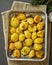 Oven baked whole crushed and crusty potato spuds with seasoning and herbs in metalic tray