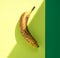 Over ripe banana with dark spots on hard light with shadows,  yellow background with green border