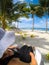 Over shoulder POV: woman in hat and dress on sun lounger on vacation at idyllic tropical beach with palm trees at Lefaga, Upolu I