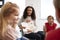 Over shoulder view of female teacher showing a picture in a book to a group of kindergarten children sitting on chairs in a classr