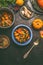 Over view of vegetarian pumpkin stew bowl with spoon and ingredients on dark rustic kitchen table background, top view.