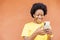 Overexcited African-American female with afro hair using a modern smartphone checking social media
