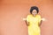 Overexcited African-American female with afro hair and yellow shirt standing against an orange wall