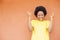 Overexcited African-American female with afro hair and yellow shirt standing against an orange wall