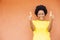 Overexcited African-American female with afro hair and yellow shirt standing against an orange wall