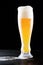 Overflowing glass of fresh cold light beer with froth flowing on the table and beautiful spilled beer on a black background with