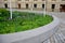 Overgrown flowerbed with white flowering perennials yellow blue tufts concrete monolith wall with bench function to arch trees