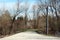 Overgrown road completely surrounded with large trees without leaves and flooded field closed with red and yellow metal ramp