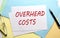 OVERHEAD COSTS text on paper sheet with chart,color paper and calculator