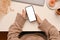 Overhead of a female in comfy sweater using a modern mobile phone in her office desk