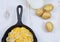 Overhead, flat lay photo. Half of a cast iron skillet filled with sliced potatoes and onions with grated cheese and bread crumbs