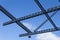Overhead grid of perforated beams and security camera against a blue sky with clouds