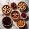 Overhead photo of different pies, tarts, and deserts on white marble table