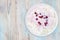 An overhead photo of fresh natural cottage cheese with cranberry yogurt in a white ceramic bowl on the wooden table. Organic eco