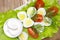 An overhead photo of vegetable salad with mayonnaise, boiled quail eggs, dill, fresh tomato and lettuce. A served salad photo from