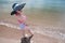 Overhead shot of a asian woman wearing a cute dark sun hat and a colorful high waist bikini dipping her toes at a brown sand beach