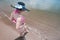 Overhead shot of a asian woman wearing a cute dark sun hat and a colorful high waist bikini dipping her toes at a brown sand beach