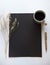 Overhead shot of a black rectangle on a white surface near a dry branch, coffee, and a pen