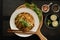 Overhead shot of a dish with noodles and vegetables in a white bowl with a chopstick on top