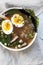Overhead vertical shot of ramen soup with eggs and vegetable leaves on a white surface