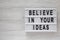 Overhead view, `Believe in your ideas` words on modern board over white wooden surface. Flat lay, from above, overhead. Copy spa