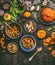 Overhead view of colorful vegetarian pumpkin stew in cooking pot and bowls with spinach and ingredients on dark rustic kitchen tab