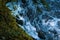 Overhead view of foamy blue water in a river with moss and grass on the shore.