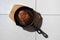 Overhead view of grilled beef steak in cast iron skillet on ceramic tile background with harsh shadow