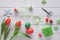 Overhead view of light wooden table with springtime decorations, wrapped gift, felt flowers, red tulips and and Easter eggs